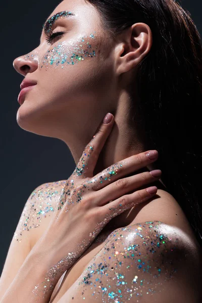 Portrait of young woman with closed eyes and glitter on eyebrows touching neck isolated on grey — Stock Photo