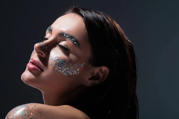 Portrait de jeune femme aux yeux fermés et aux paillettes sur les sourcils isolés sur gris — Photo de stock