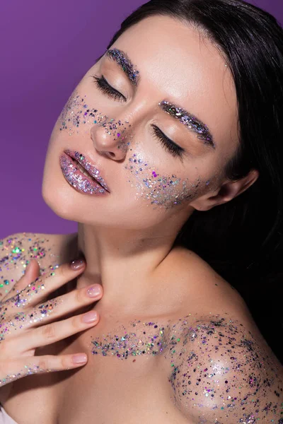 Sensual woman with closed eyes and glitter on face isolated on purple — Stock Photo