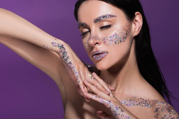 Sensual woman with closed eyes and glitter on face posing isolated on purple — Stock Photo