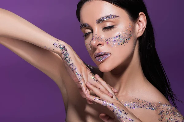 Femme sensuelle avec les yeux fermés et des paillettes sur le visage posant isolé sur violet — Photo de stock