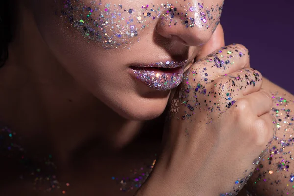 Ausgeschnittene Ansicht einer jungen Frau mit Glitzern auf den Lippen und Wangen vereinzelt auf lila — Stockfoto