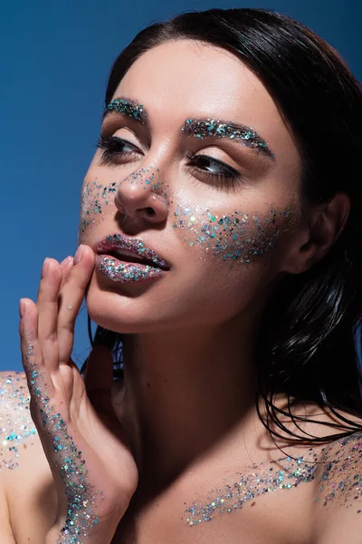 Portrait of brunette young woman with glitter on lips and cheeks isolated on blue — Stock Photo