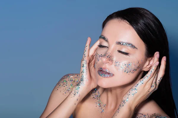 Overhead view of brunette young woman with glitter on lips and cheeks isolated on blue — Stock Photo