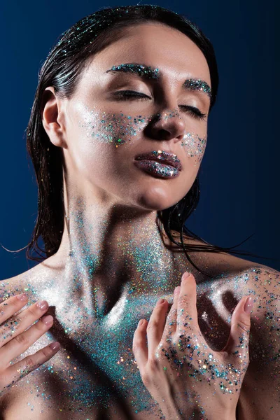 Портрет молодої жінки із закритими очима та блискучим блиском на тілі ізольовано на синьому — стокове фото