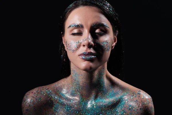 Portrait of young woman with closed eyes and blue sparking glitter on body isolated on black — Stock Photo