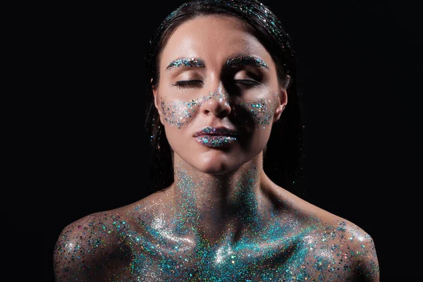 Portrait de jeune femme aux yeux fermés et étincelle bleue paillettes sur le corps isolé sur noir — Photo de stock