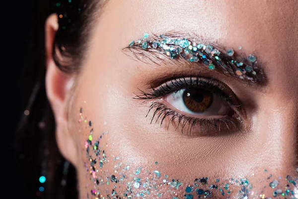 Vue rapprochée de la jeune femme avec étincelle paillettes sur le sourcil et le visage isolé sur noir — Photo de stock