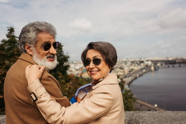 Happy senior woman in stylish sunglasses hugging bearded husband in beige coat — Stock Photo