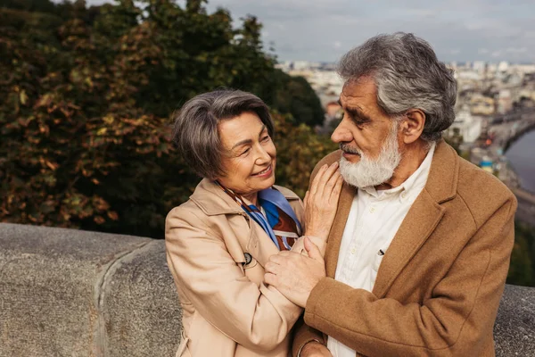 Seniorin stützt sich auf die Schulter ihres Mannes im Mantel, während sie einander ansieht — Stockfoto