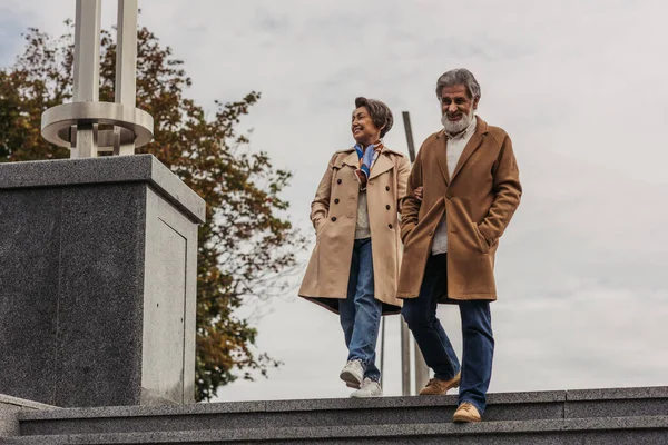 Полная длина стильный старший мужчина в пальто ходить по лестнице с руками в карманах рядом счастливая жена — стоковое фото