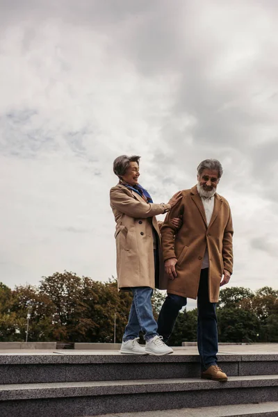 Full length of happy senior woman in coat walking on stairs with stylish husband — Stock Photo