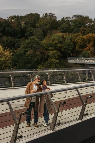 Full length of happy senior woman and bearded man standing near bridge guard rail — Stock Photo