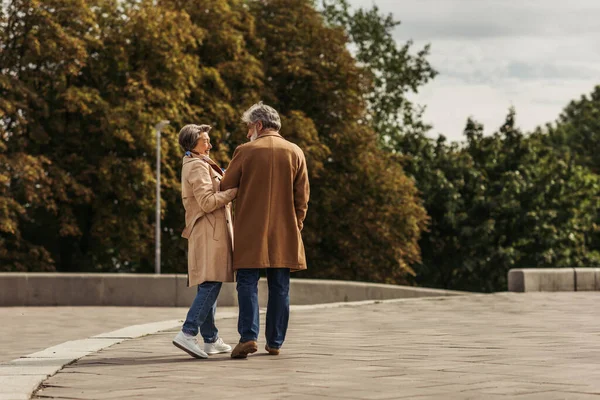 Volle Länge der fröhlichen Seniorin umarmt bärtigen Mann im Mantel und geht draußen — Stockfoto