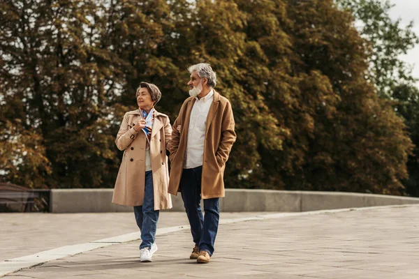 Piena lunghezza di donna anziana sorridente e uomo barbuto in cappotto a piedi al di fuori — Foto stock