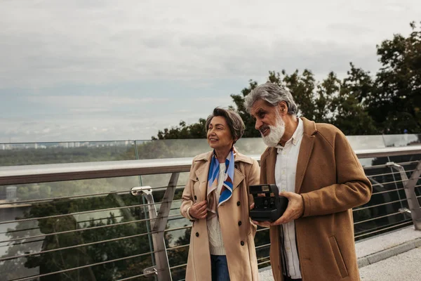 Heureux homme âgé tenant caméra vintage près de femme gaie sur le pont — Photo de stock