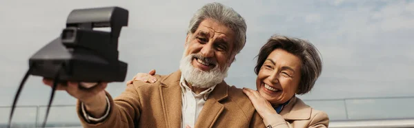 Happy senior man taking selfie with cheerful wife on vintage camera, banner — Stock Photo