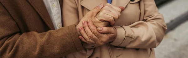 Vista ritagliata dell'uomo anziano che tiene la mano della moglie in trench all'esterno, banner — Foto stock