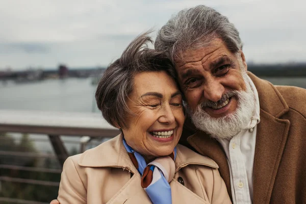 Portrait of happy senior couple in beige coats smiling outside — Stock Photo