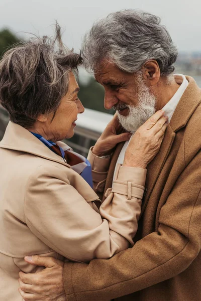 Счастливая пожилая женщина обнимает бородатого мужа в бежевом пальто — стоковое фото