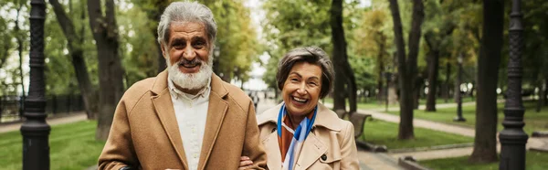 Glückliche Seniorin und stilvoller Mann in Mänteln lächelnd im grünen Park, Banner — Stockfoto