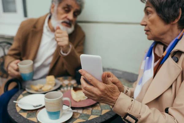 Seniorin hält Smartphone beim Brunch mit Ehemann auf Caféterrasse — Stockfoto