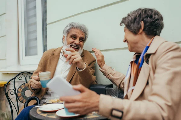 Alegre pareja de ancianos riendo durante el almuerzo en la terraza de la cafetería - foto de stock