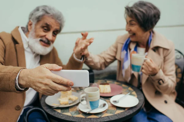 Coppia anziana offuscata e felice avendo videochiamata durante la colazione sulla terrazza del caffè — Foto stock