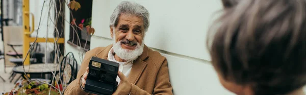 Allegro uomo anziano con barba che tiene la fotocamera vintage vicino alla moglie, banner — Foto stock