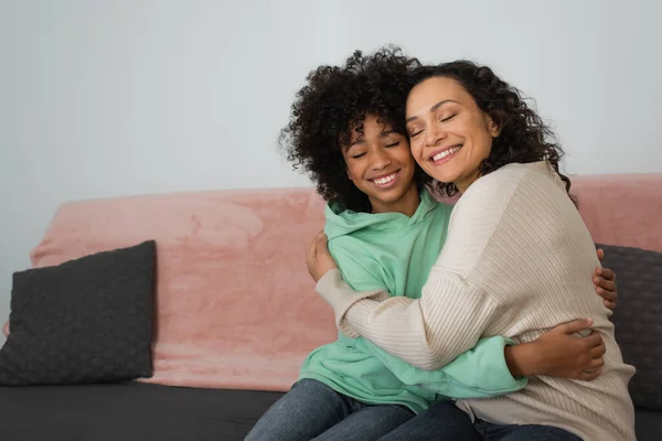 Happy african american mother and daughter hugging while sitting on couch — Stock Photo