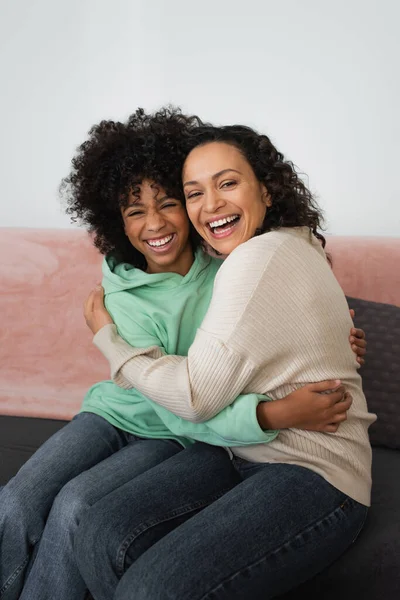 Excité afro-américaine mère et fille câlins tandis que assis sur le canapé — Photo de stock