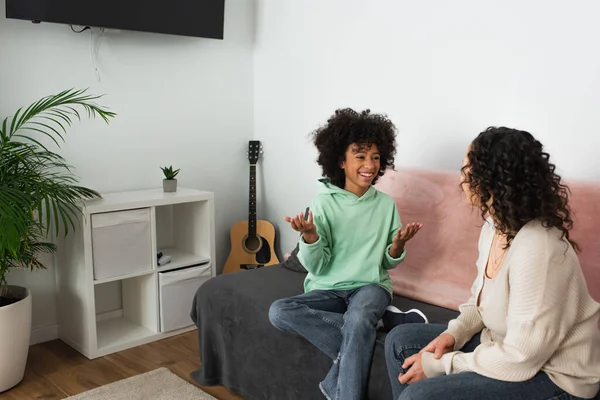 Ricci africano americano ragazza sorridente mentre gesticolando vicino madre in soggiorno — Foto stock