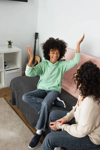 Menina americana africana feliz sorrindo enquanto gesticulando perto de mãe encaracolada na sala de estar — Fotografia de Stock