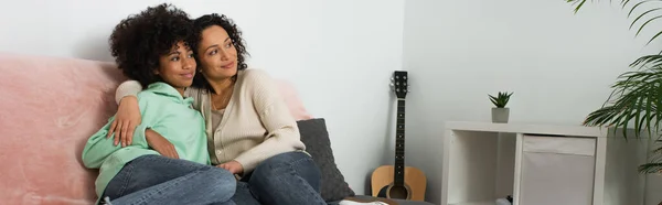 Happy african american mother hugging cheerful preteen daughter in living room, banner — Stock Photo