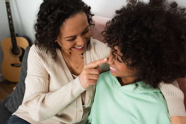 Hochwinkelaufnahme einer glücklichen afrikanisch-amerikanischen Mutter, die im Wohnzimmer die Nase einer fröhlichen Tochter berührt — Stockfoto