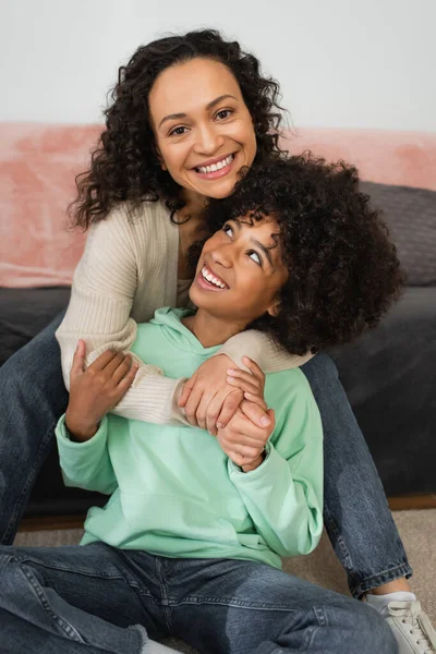 Feliz africano americano mujer sonriendo mientras abrazando preadolescente hija - foto de stock