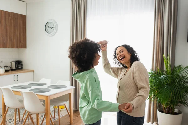 Cheerful african american woman holding hands while dancing with curly preteen daughter — Stock Photo