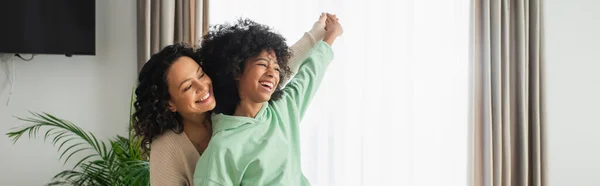 Весела афроамериканська мати і дочка тримаються за руки, посміхаючись вдома, банер — стокове фото