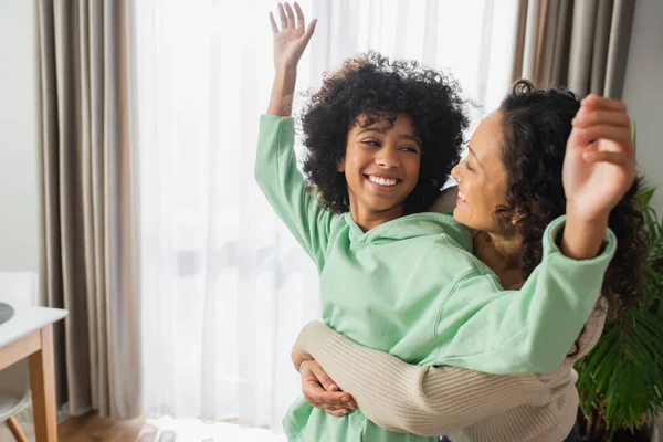Весела афроамериканка, яка обіймає щасливу доньку - підлітка з піднятими руками. — стокове фото
