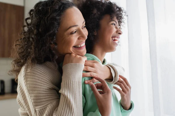 Ritratto di allegra donna africana americana sorridente mentre abbraccia gioiosa figlia preadolescente — Foto stock