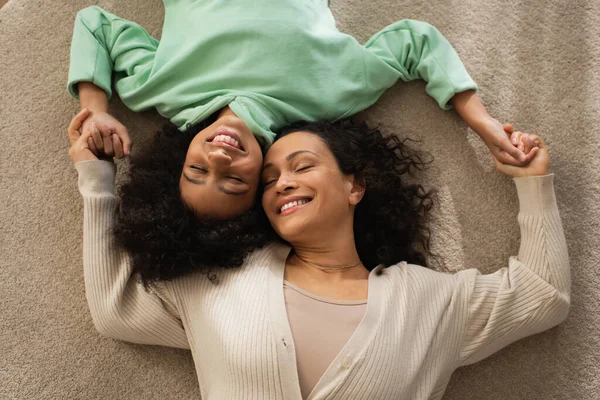 Draufsicht auf lächelndes afrikanisch-amerikanisches Mädchen, das mit fröhlicher Mutter auf Teppich liegt — Stockfoto