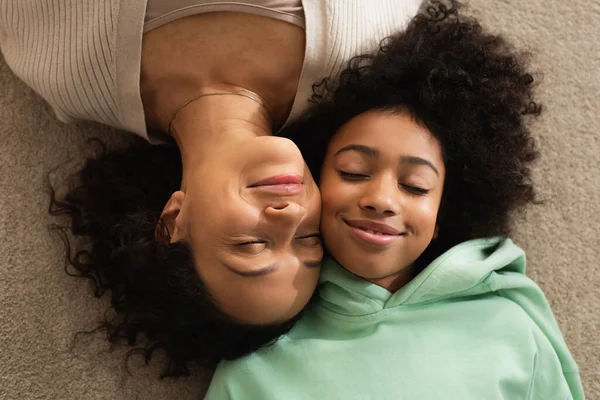 Blick von oben auf glückliches afrikanisch-amerikanisches Mädchen, das mit fröhlicher Mutter auf Teppich liegt — Stockfoto