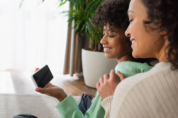 Feliz Africano americano preteen menina segurando smartphone com tela em branco perto de mãe positiva — Fotografia de Stock