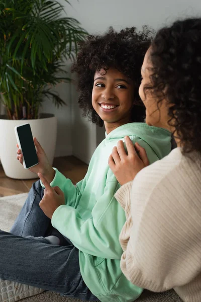 Щаслива афро-американська дівчина тримає смартфон з порожнім екраном біля кучерявої матері — стокове фото