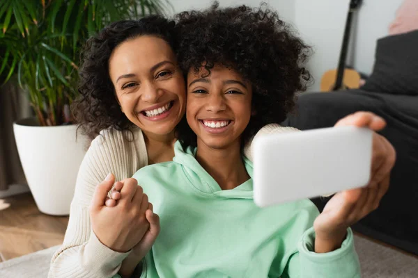 Alegre afro-americana mãe tomando selfie com alegre pré-adolescente filha no smartphone — Fotografia de Stock