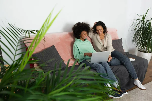 Alegre afroamericano preadolescente chica y feliz mujer viendo película en portátil - foto de stock