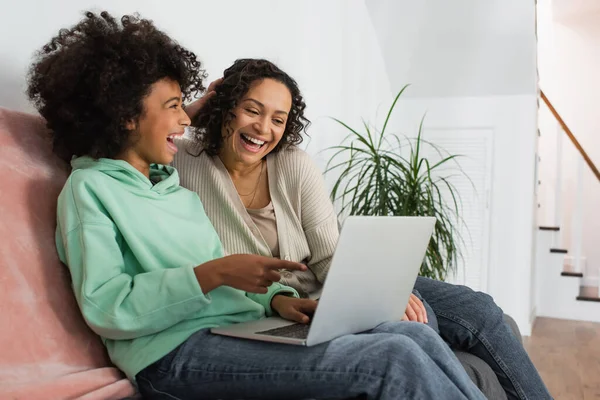 Alegre Africano americano preteen menina apontando para laptop perto de mãe feliz — Fotografia de Stock