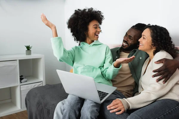 Feliz afroamericano preadolescente chica gesto cerca de los padres en sala de estar - foto de stock