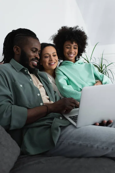 Familia afroamericana feliz viendo la película en el ordenador portátil en la sala de estar - foto de stock