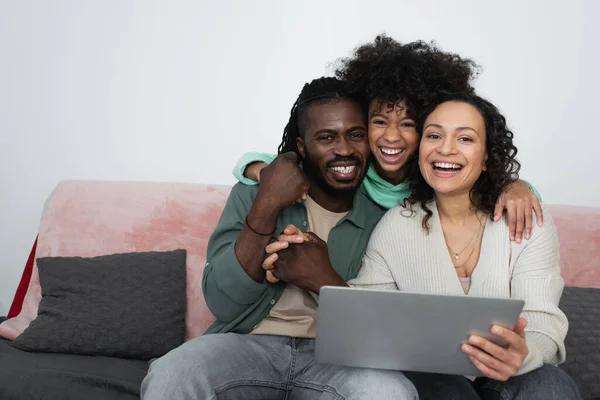 Cheerful african american family smiling while looking at camera near laptop in living room — Stock Photo